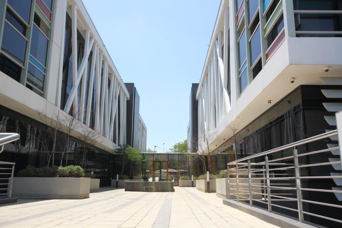 Modern office complex courtyard featuring paved walkways, integrated planters, and contemporary architectural facade design with glass and steel elements.