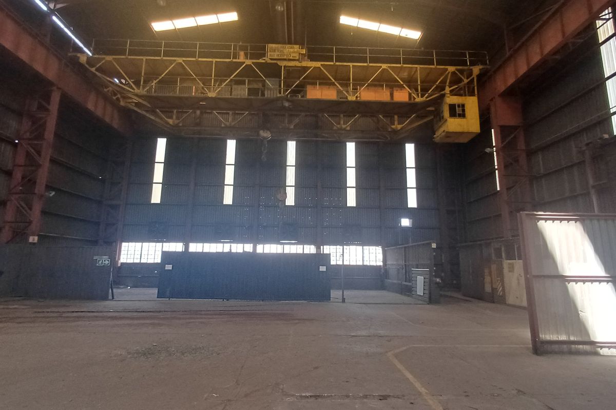 Large industrial warehouse space featuring a high-clearance ceiling with an integrated overhead gantry crane, concrete flooring, and expansive metal-clad walls.