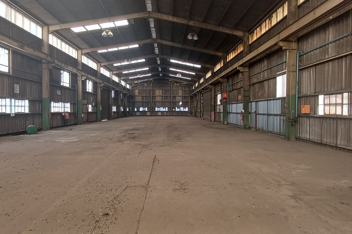 Expansive industrial warehouse space featuring a high-clearance steel portal frame, concrete flooring, and natural light through integrated skylights.