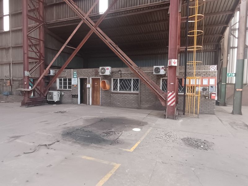 Large industrial warehouse space featuring a central brick office block, exposed steel structural framing, and concrete flooring.