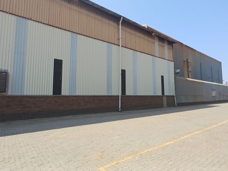 Exterior view of an industrial warehouse building featuring corrugated metal cladding, a brick base, and a paved driveway area.