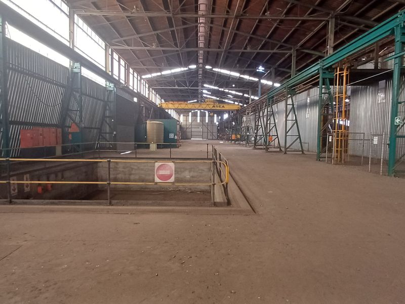 Large industrial warehouse space featuring high ceilings, overhead gantry crane, corrugated metal walls, and a recessed concrete inspection pit.