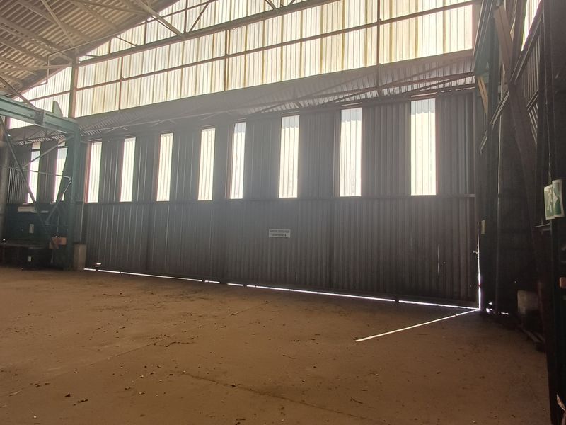 Spacious industrial utility area featuring high ceilings, corrugated metal walls, concrete flooring, and a large sliding access door for heavy equipment.