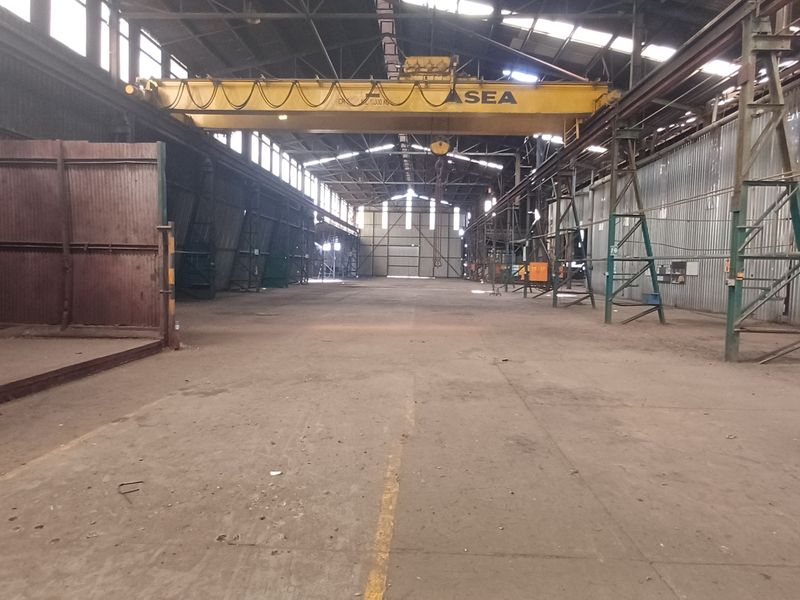 Expansive industrial warehouse space featuring high ceilings, concrete flooring, and an integrated overhead crane system, suitable for heavy manufacturing or storage operations.