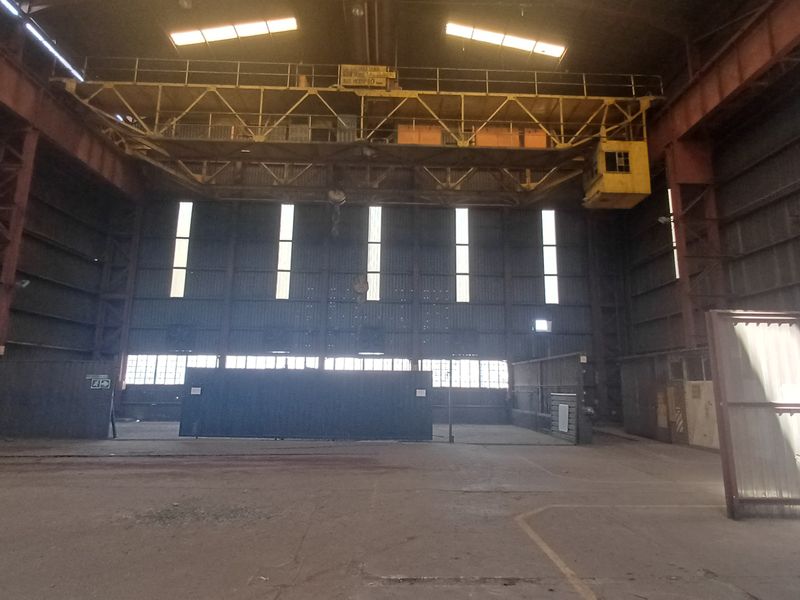 Large industrial warehouse space featuring a high-clearance ceiling with an integrated overhead gantry crane, concrete flooring, and expansive metal-clad walls.