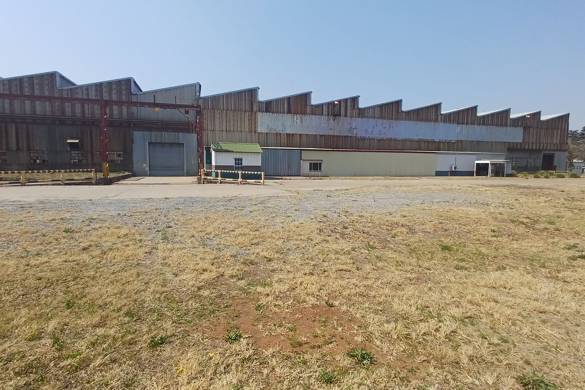 Large industrial warehouse facility featuring a sawtooth roof design, corrugated metal cladding, and a spacious concrete yard area.