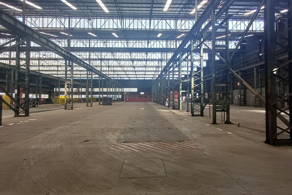 Expansive industrial warehouse space featuring high ceilings, exposed steel structural framework, and durable concrete flooring, suitable for large-scale storage or manufacturing operations.
