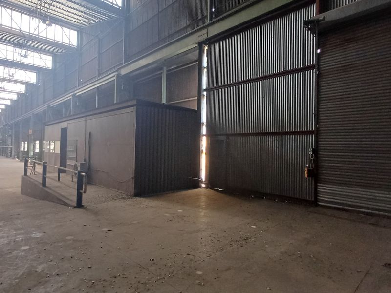 Expansive industrial warehouse space featuring high ceilings, steel structural framing, corrugated metal walls, and a large roller shutter door for vehicle access.