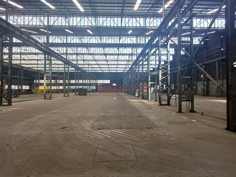 Expansive industrial warehouse space featuring high ceilings, exposed steel structural framework, and durable concrete flooring, suitable for large-scale storage or manufacturing operations.