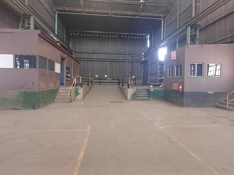 Large industrial warehouse space featuring a central loading ramp, steel frame construction, and integrated office enclosures with concrete flooring.
