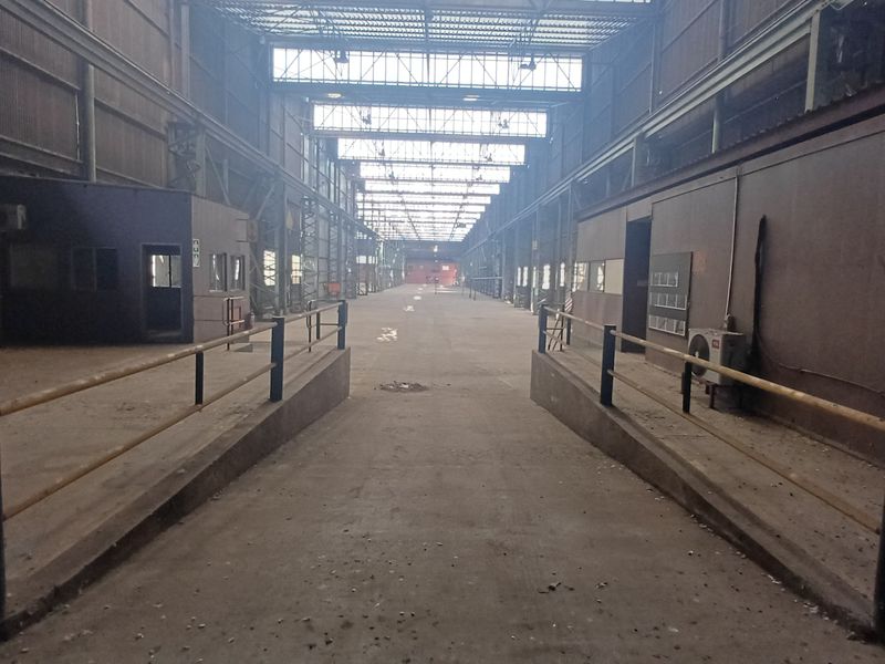 Expansive industrial warehouse space featuring high steel truss ceilings, concrete flooring, and a central loading ramp with safety railings.