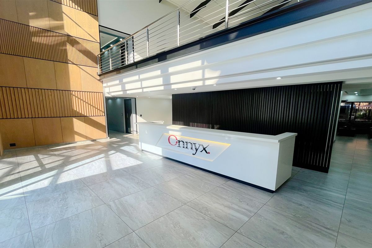 Modern office entrance featuring a sleek built-in reception desk, double-volume ceiling, mezzanine level with stainless steel balustrade, and contemporary timber and slatted wall finishes.
