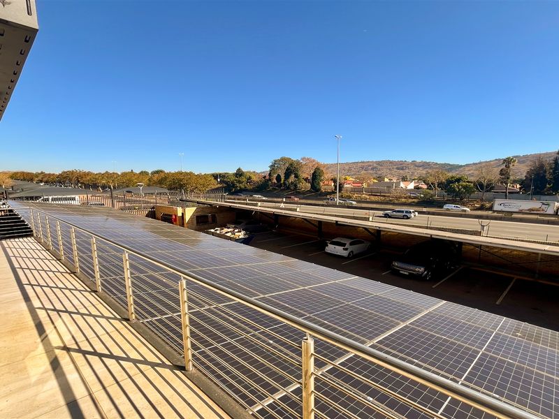 Spacious balcony featuring tiled flooring, a stainless steel balustrade, and an extensive solar panel installation overlooking the parking area and surrounding landscape.