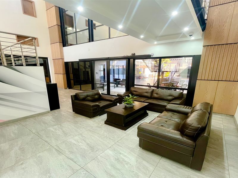 Modern double-volume office reception area featuring high ceilings, wood paneling, large format floor tiles, and extensive glass sliding doors leading to an outdoor space.