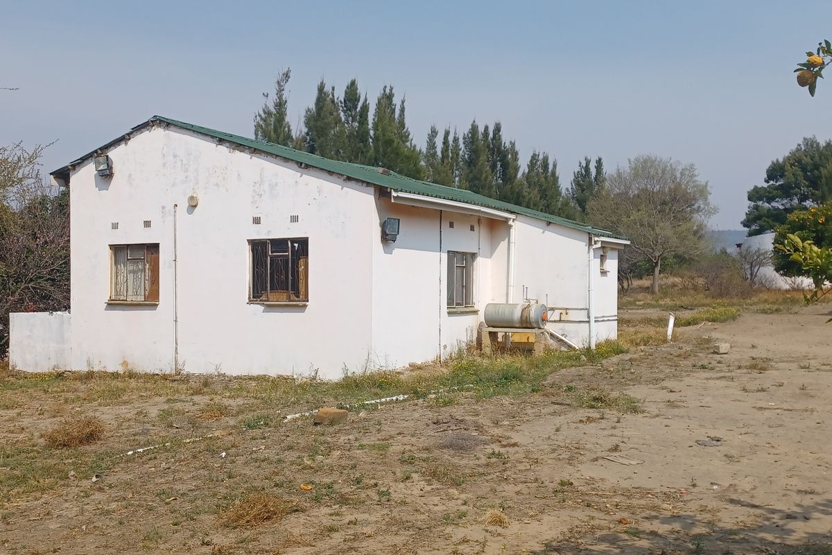 Rear view of a farm dwelling featuring a metal roof, external geyser, and security bars on windows, set on a large rural plot.