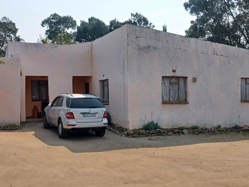 Front elevation of a single-story farm dwelling featuring a concrete driveway and weathered exterior walls requiring maintenance and cosmetic updates.