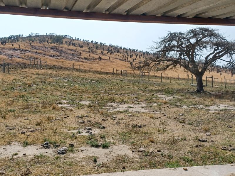 A covered outdoor patio area overlooking a rural landscape with wire fencing and natural terrain.