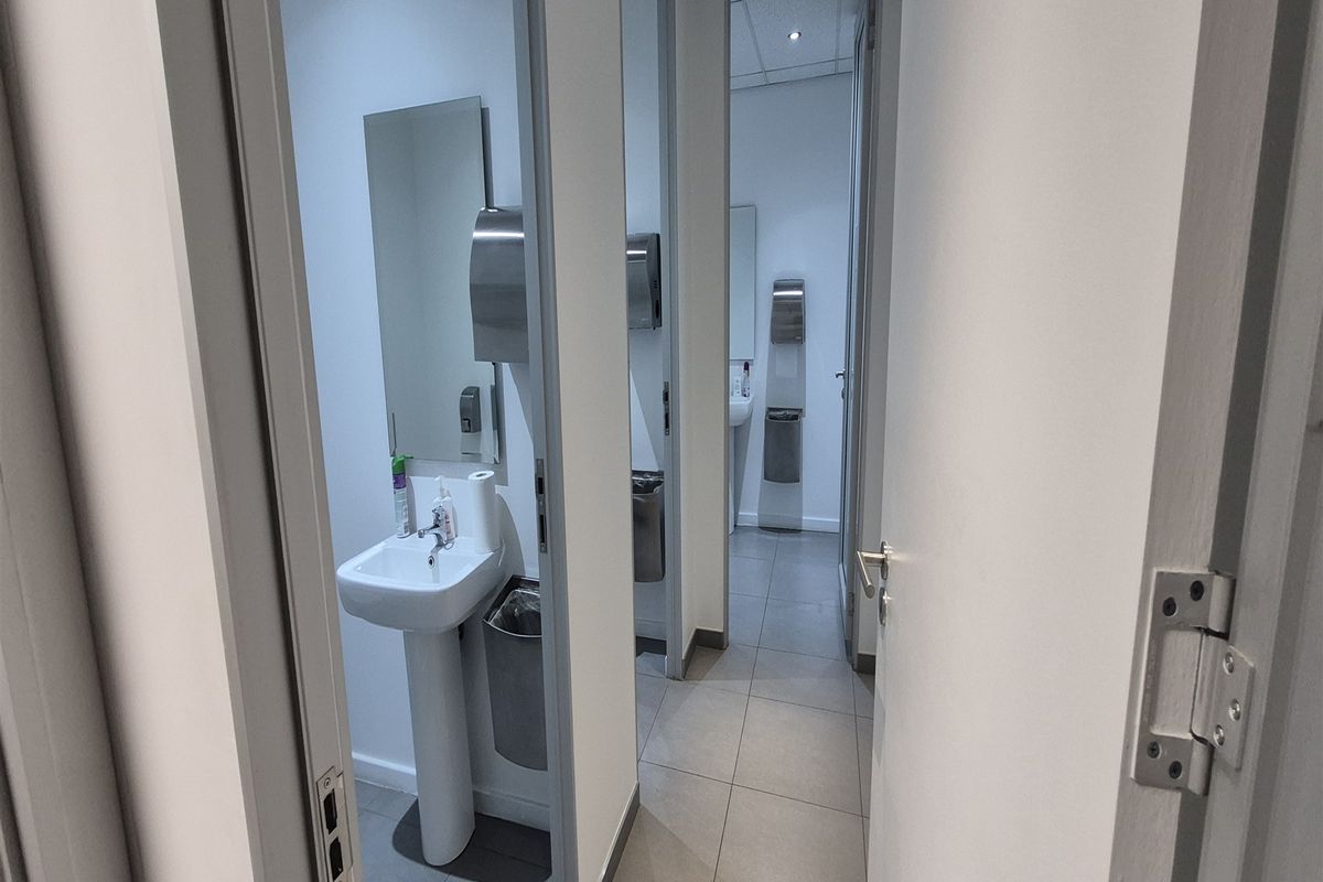 A clean, functional office restroom facility featuring multiple individual stalls with pedestal sinks, tiled flooring, and modern stainless steel fixtures.