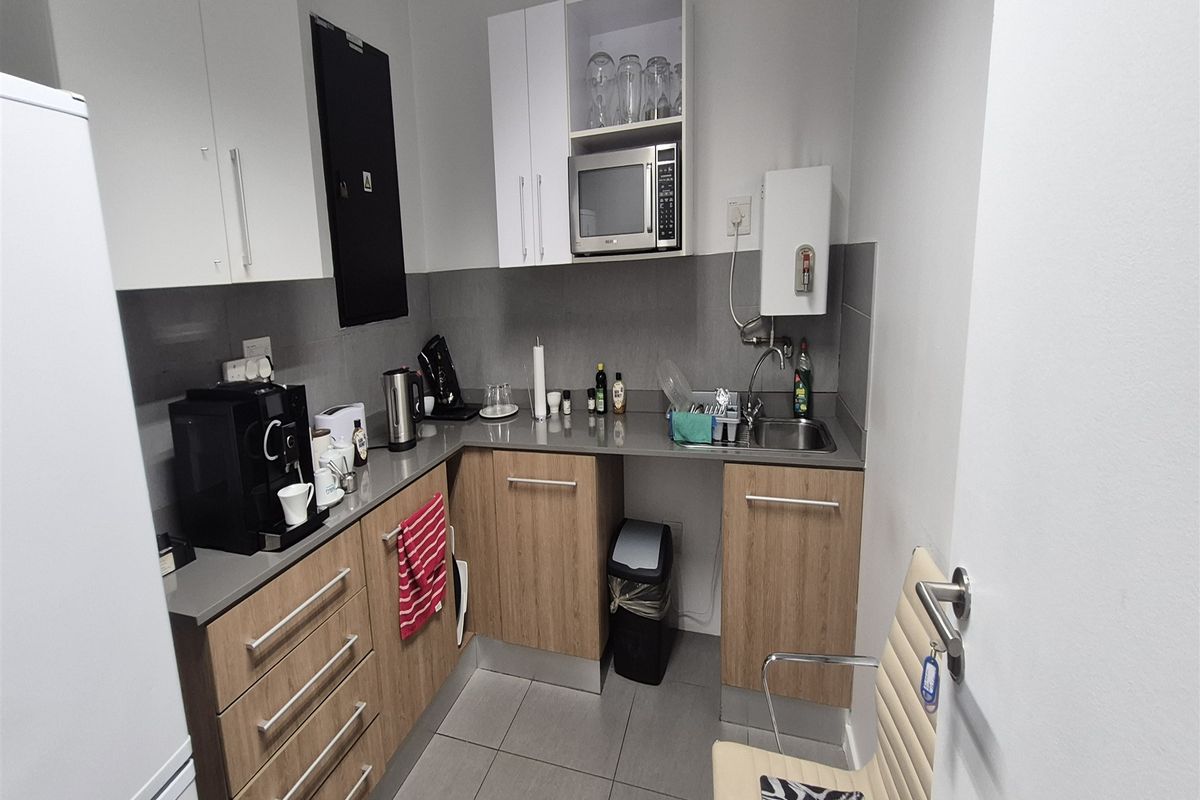 A compact office kitchenette featuring modern wood-grain cabinetry, grey stone-look countertops, a stainless steel sink, and a built-in microwave.