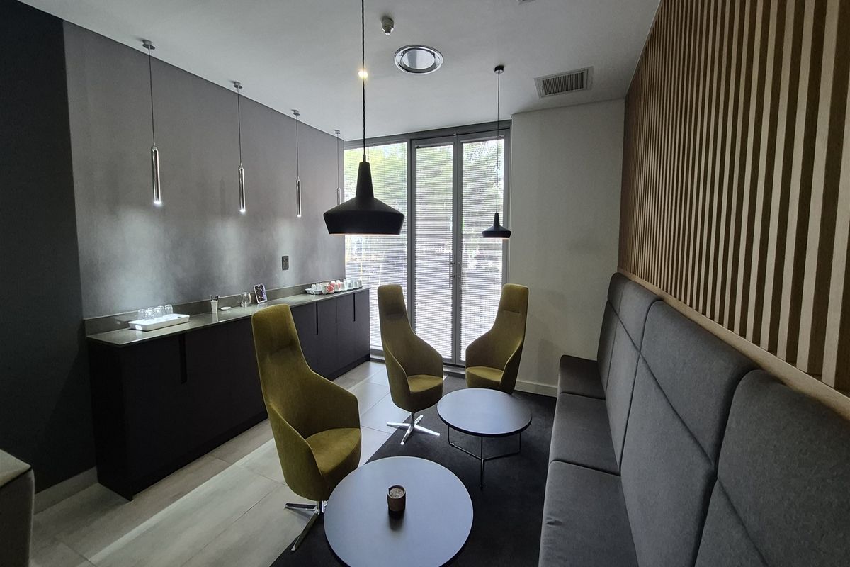 Modern office breakout area featuring built-in cabinetry, contemporary pendant lighting, timber slat wall paneling, and large glass doors providing natural light.