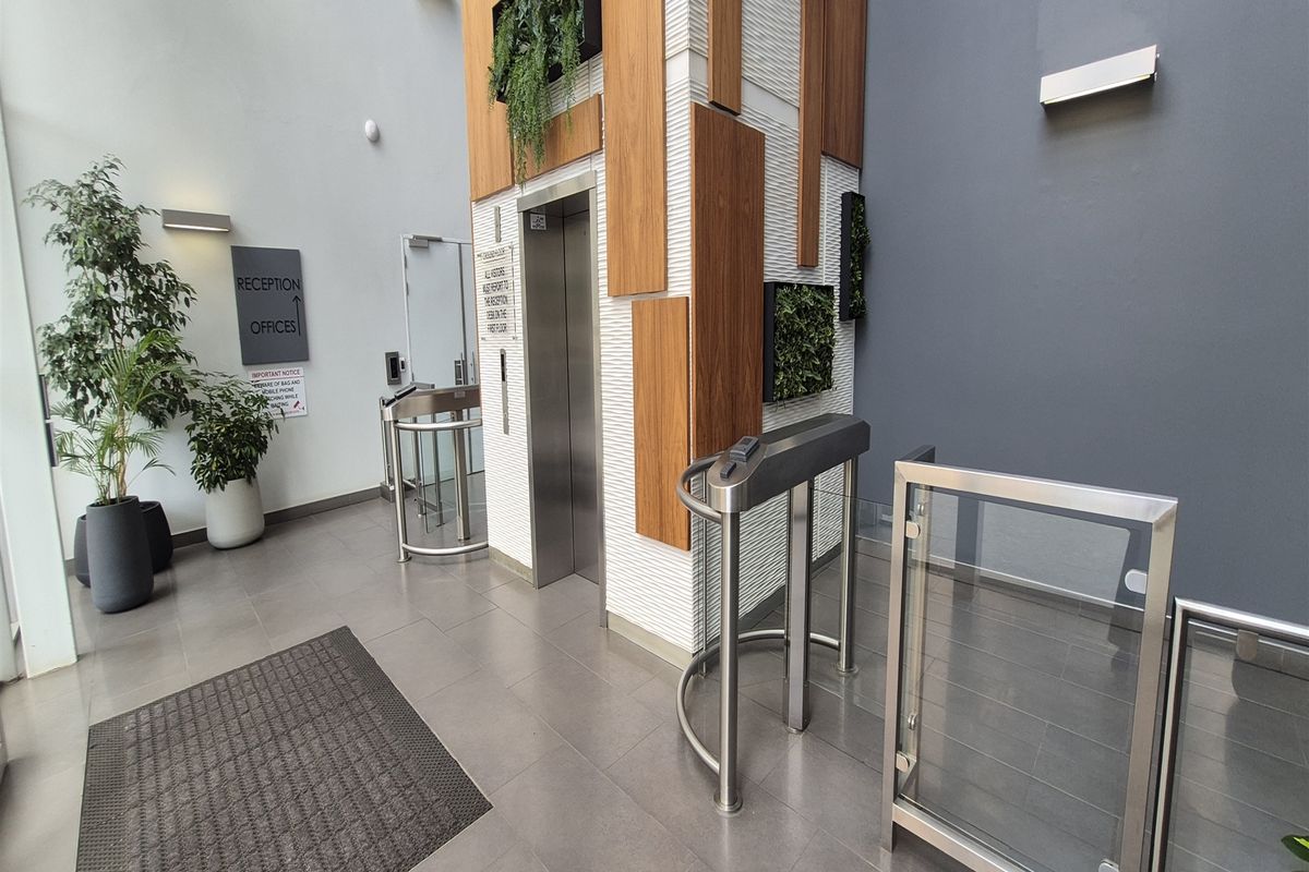 Modern office building lobby featuring a secure elevator access point with contemporary wood-panelled cladding, glass turnstiles, and sleek tiled flooring.
