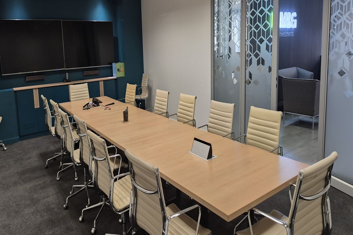 A professional boardroom featuring a large wooden conference table, integrated wall-mounted screens, and glass partition walls with decorative frosted detailing.