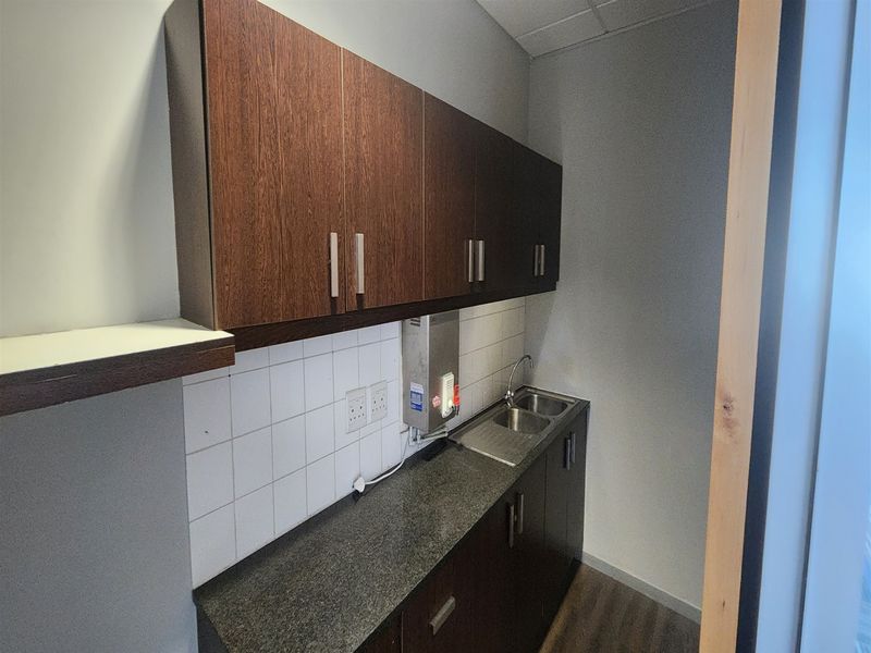 Compact office kitchenette featuring dark wood-look cabinetry, granite countertops, a stainless steel double sink, and a tiled backsplash.