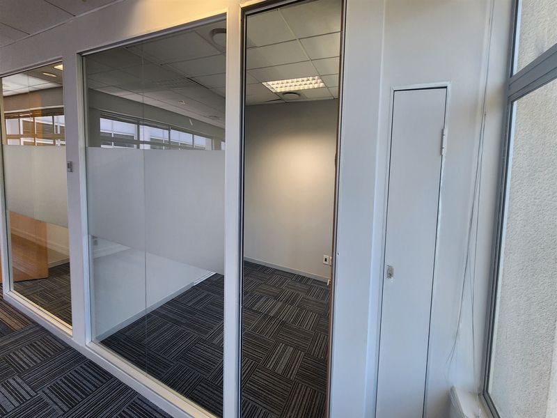 A modern, empty office space featuring glass partitioning, suspended ceilings with recessed lighting, and durable carpet tiles, ideal for a professional workspace.
