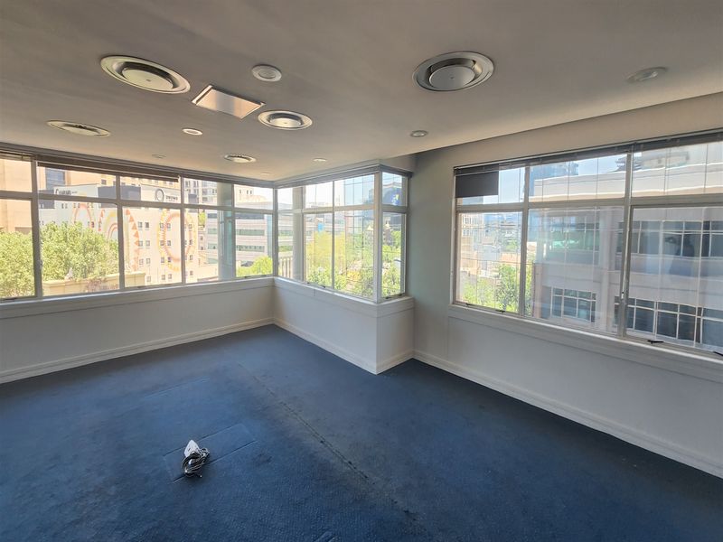 A bright, empty office space featuring large wrap-around windows providing ample natural light and recessed ceiling air conditioning vents.