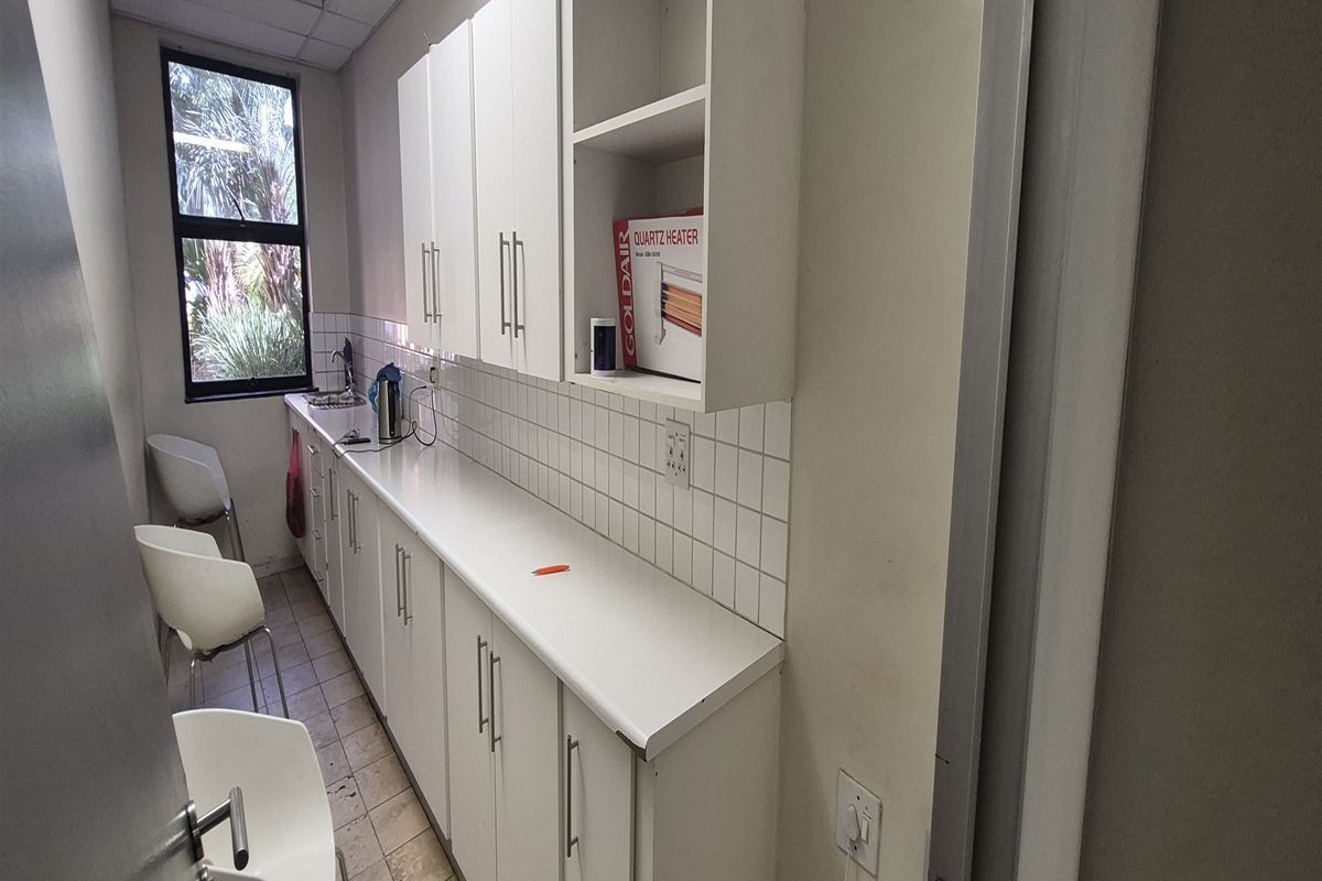 A functional office kitchenette featuring white cabinetry, tiled backsplash, and a stainless steel sink, providing a convenient space for staff refreshments.