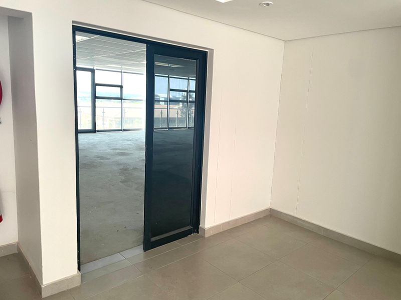 A bright, empty office space featuring modern tiled flooring, recessed lighting, and a sliding glass door leading to an adjacent open-plan work area.