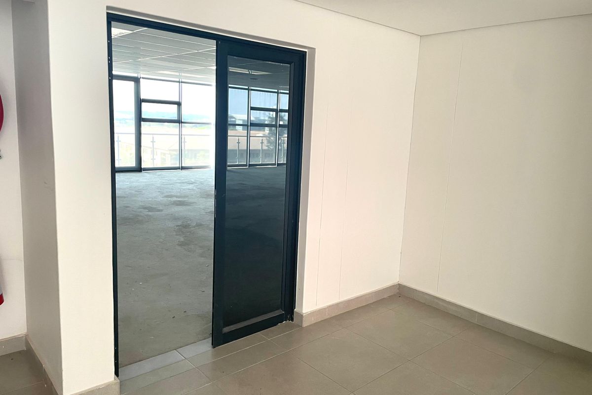 A bright, empty office space featuring modern tiled flooring, recessed lighting, and a sliding glass door leading to an adjacent open-plan work area.