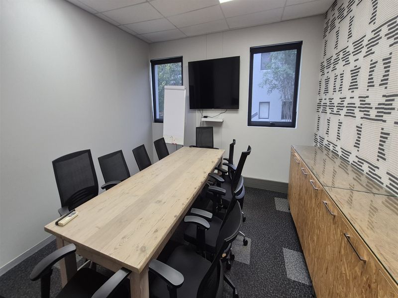 A functional office meeting room featuring built-in cabinetry, carpeted flooring, and natural light through casement windows.