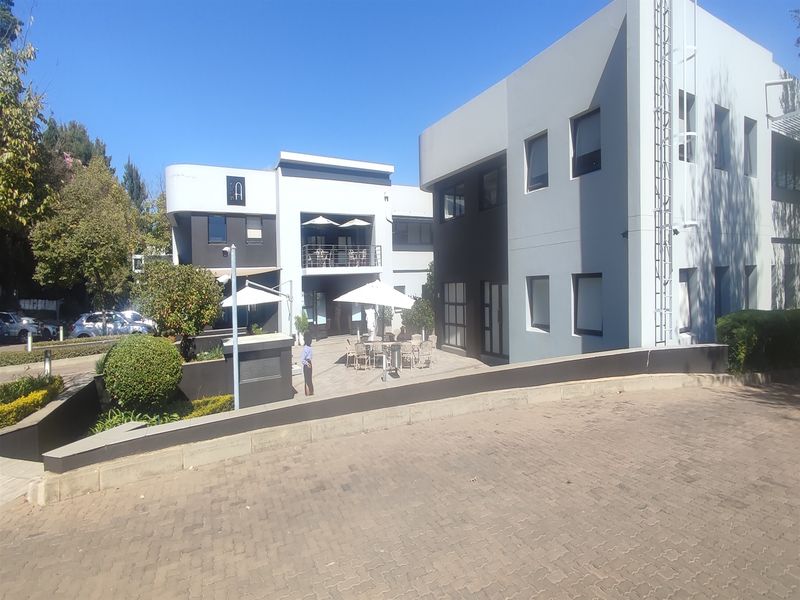 Modern multi-story office building exterior featuring a paved driveway, landscaped retaining walls, and an accessible balcony area.