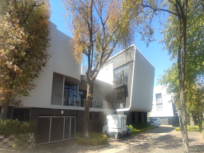A modern office building featuring a contemporary architectural design with large glass windows, balconies, and integrated louvre screens set in a landscaped environment.