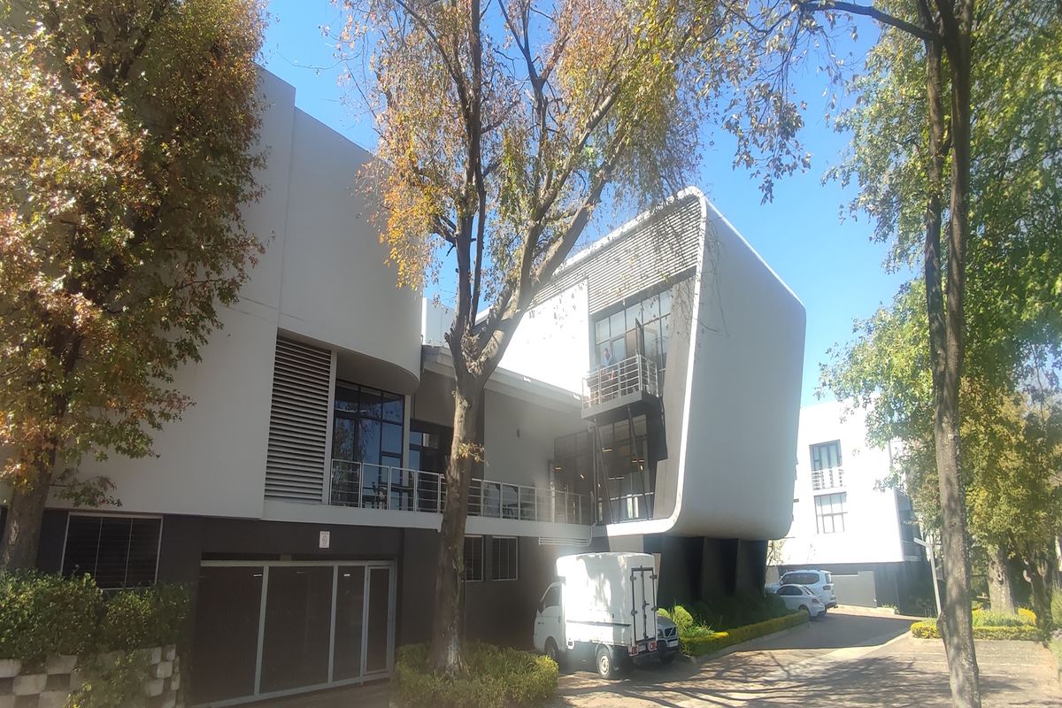 A modern office building featuring a contemporary architectural design with large glass windows, balconies, and integrated louvre screens set in a landscaped environment.