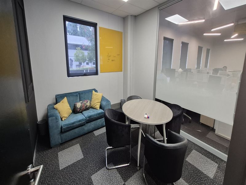 A modern office meeting room featuring a glass partition wall, recessed lighting, and professional carpet tiles.