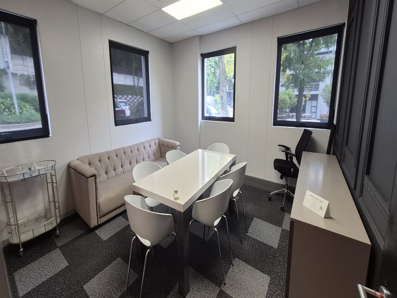 A well-lit office space featuring modern carpet tiles, suspended ceiling, and large windows providing natural light.