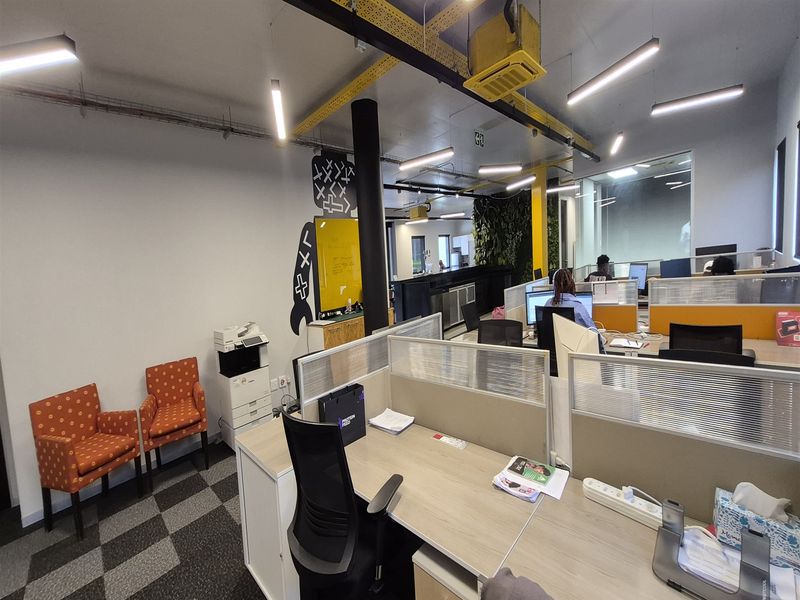 Open-plan office space featuring modular workstations, exposed ceiling infrastructure, linear lighting, and a decorative vertical garden wall.
