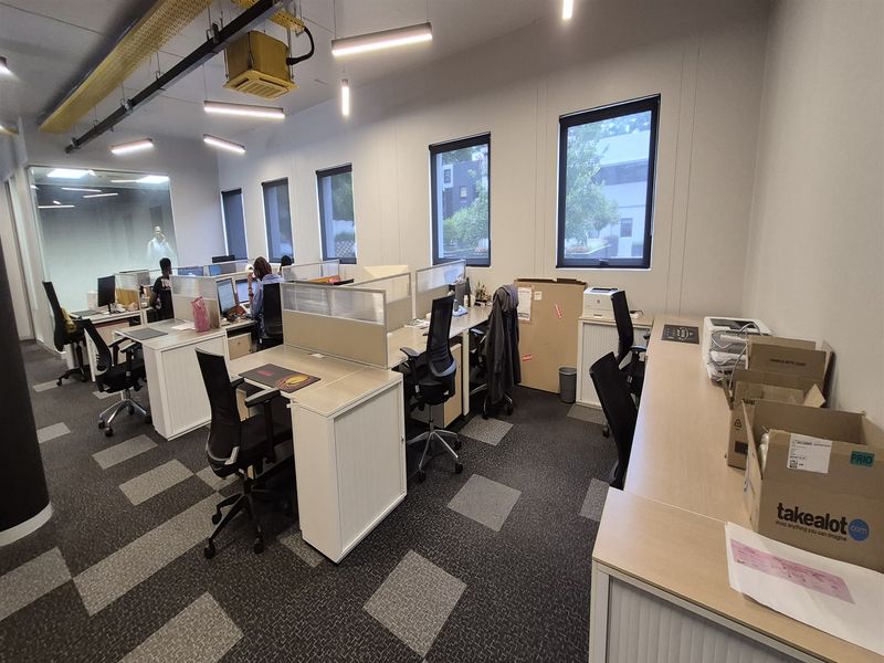 Modern open-plan office space featuring built-in workstations, partition screens, suspended lighting, and carpet tiles, providing a functional and professional work environment.