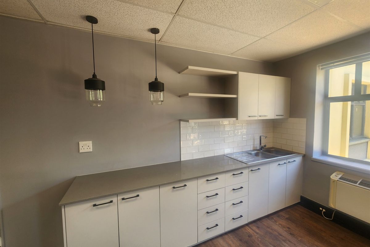 A modern office kitchenette featuring sleek cabinetry, stone countertops, a stainless steel sink, subway tile backsplash, and contemporary pendant lighting.