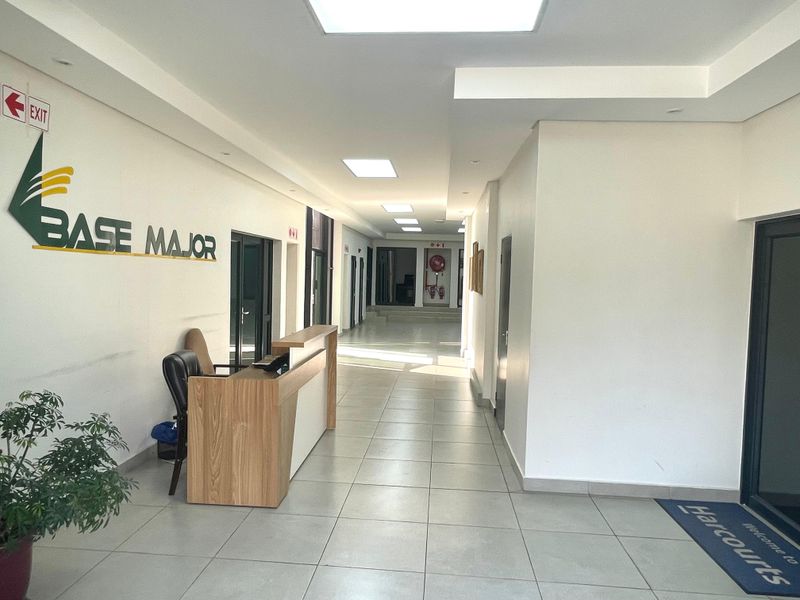 A bright, modern office hallway featuring tiled flooring, recessed ceiling lighting, and clear directional signage leading to multiple office suites.