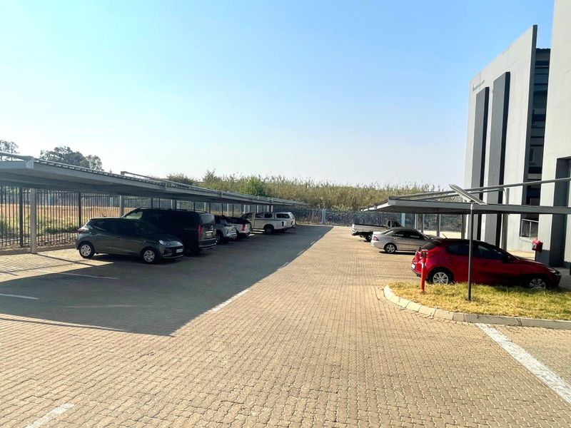 Exterior view of a commercial office property featuring a paved parking lot with multiple covered parking bays and perimeter security fencing.