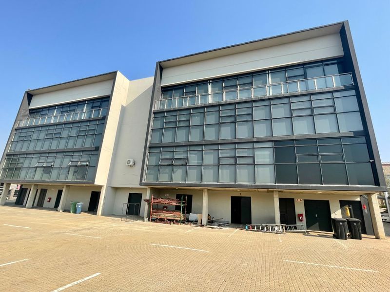 Modern multi-story office building featuring a glass curtain wall facade and an expansive paved parking area.