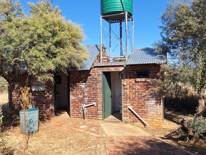 A rustic brick utility outbuilding on a farm, featuring an elevated water storage tank and external plumbing infrastructure.