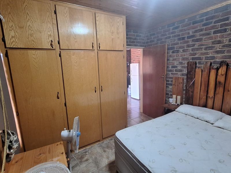 A bedroom featuring built-in wooden cupboards, exposed brick wall detailing, and tiled flooring, offering a rustic farm-style aesthetic.