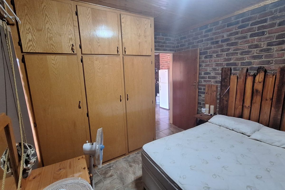A bedroom featuring built-in wooden cupboards, exposed brick wall detailing, and tiled flooring, offering a rustic farm-style aesthetic.