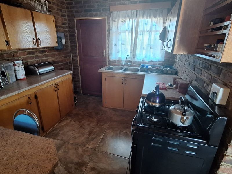 A rustic kitchen featuring exposed brick walls, wooden cabinetry, tiled flooring, and a double basin sink, offering a functional layout with a classic farm-style aesthetic.