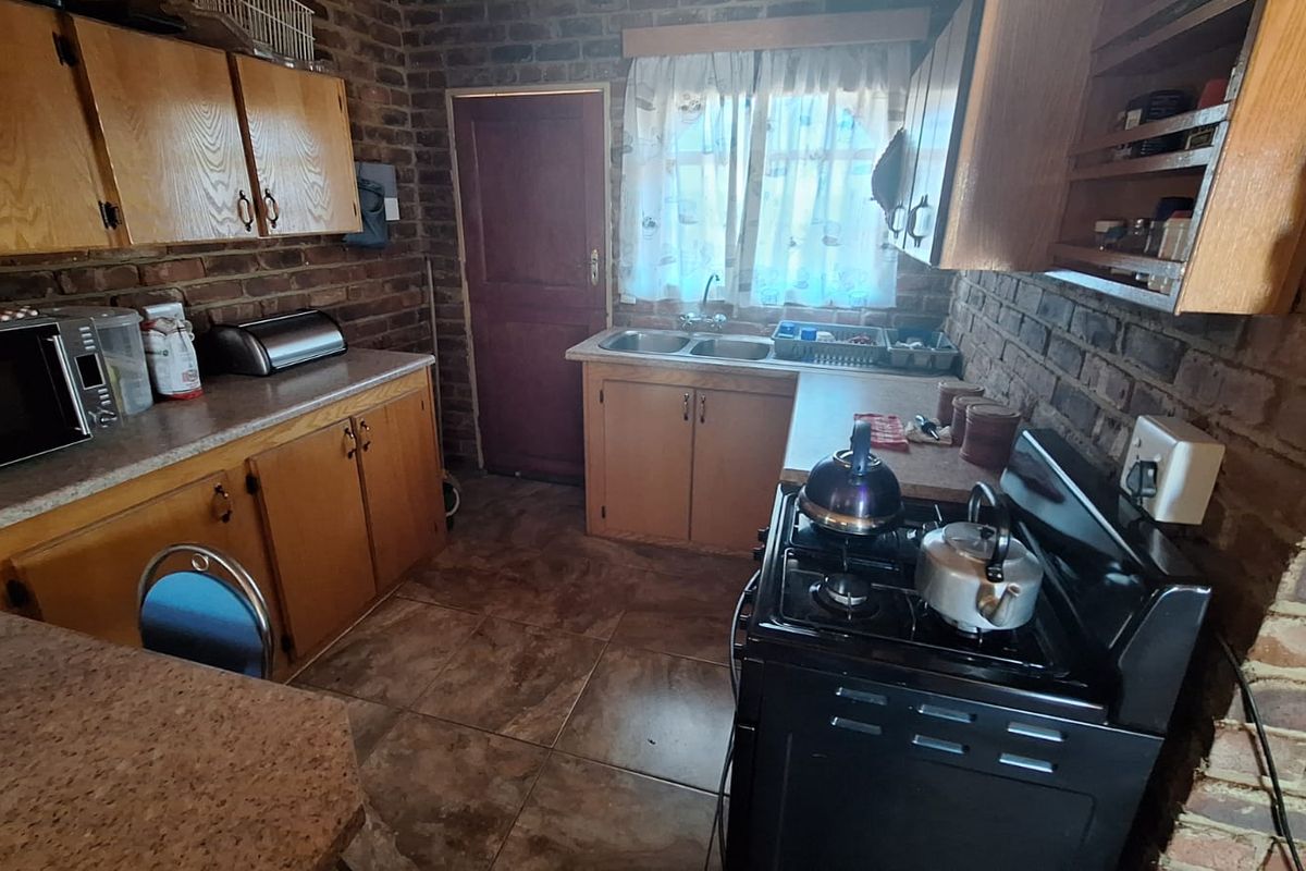 A rustic kitchen featuring exposed brick walls, wooden cabinetry, tiled flooring, and a double basin sink, offering a functional layout with a classic farm-style aesthetic.