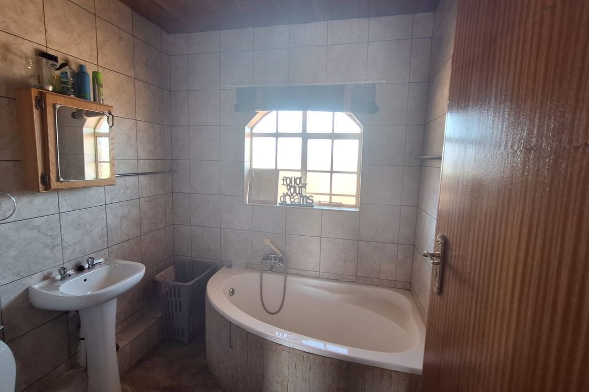 A functional bathroom featuring a corner bathtub, pedestal basin, and wall-mounted medicine cabinet with tiled finishes throughout.